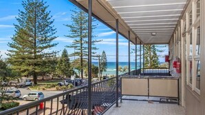 Un balcon avec vue sur l’océan et les arbres.