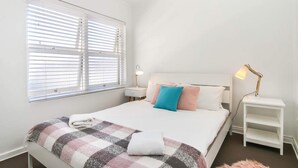 Une chambre à coucher comprenant un lit, deux tables de chevet, une commode et une fenêtre avec des stores.