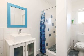 A bathroom with a white sink, a blue-framed mirror, a shower with a blue checkered curtain, and a toilet.
