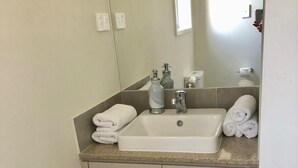 Ein Badezimmer mit weißem Waschbecken, zwei Handtuchhaltern, einem Spiegel und einer Toilette.