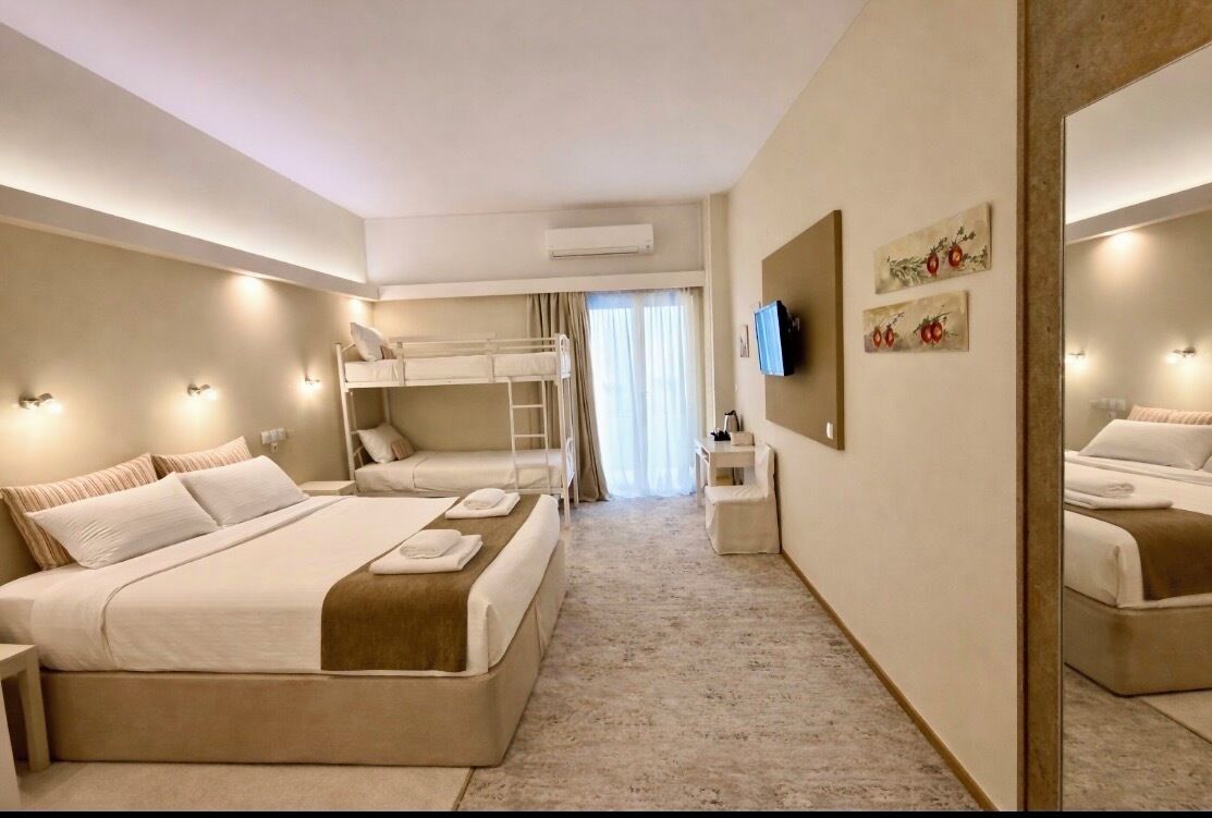A hotel room with a bunk bed, a flat bed, a TV, and a mirror.