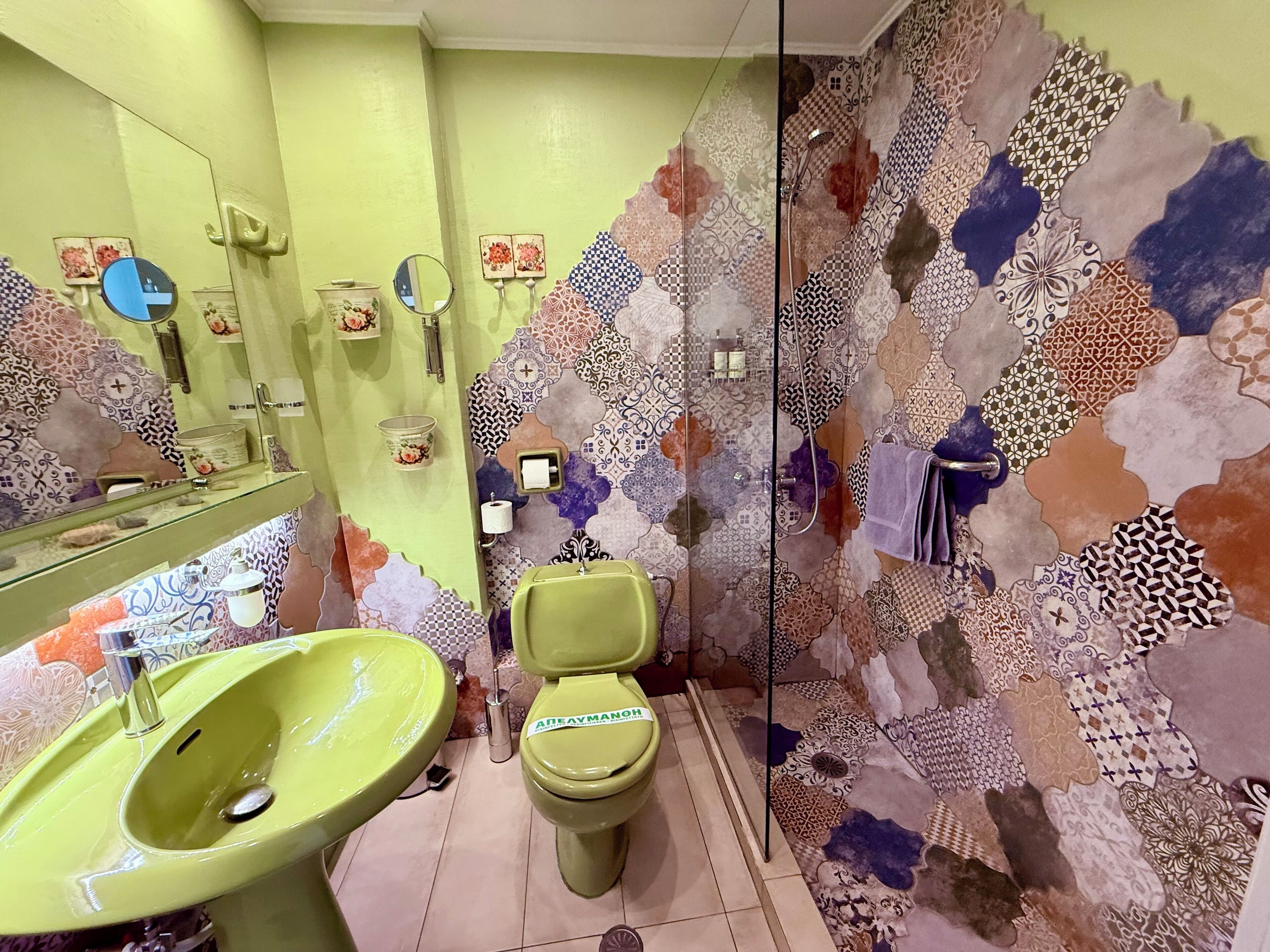 Un baño con un lavabo verde, inodoro y ducha con pared decorada.