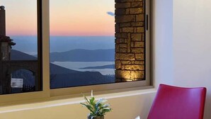 Una habitación con un ventanal grande, una mesa pequeña con una planta, una silla roja y una lámpara en la pared.