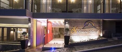 The exterior of Sidimos Hotel with a prominent entrance, a balcony, and a well-lit facade.