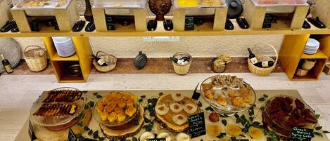 Una vitrina de panadería con diversos productos horneados y postres, como tartas, pasteles y dulces, dispuestos en estantes de madera y una mesa.