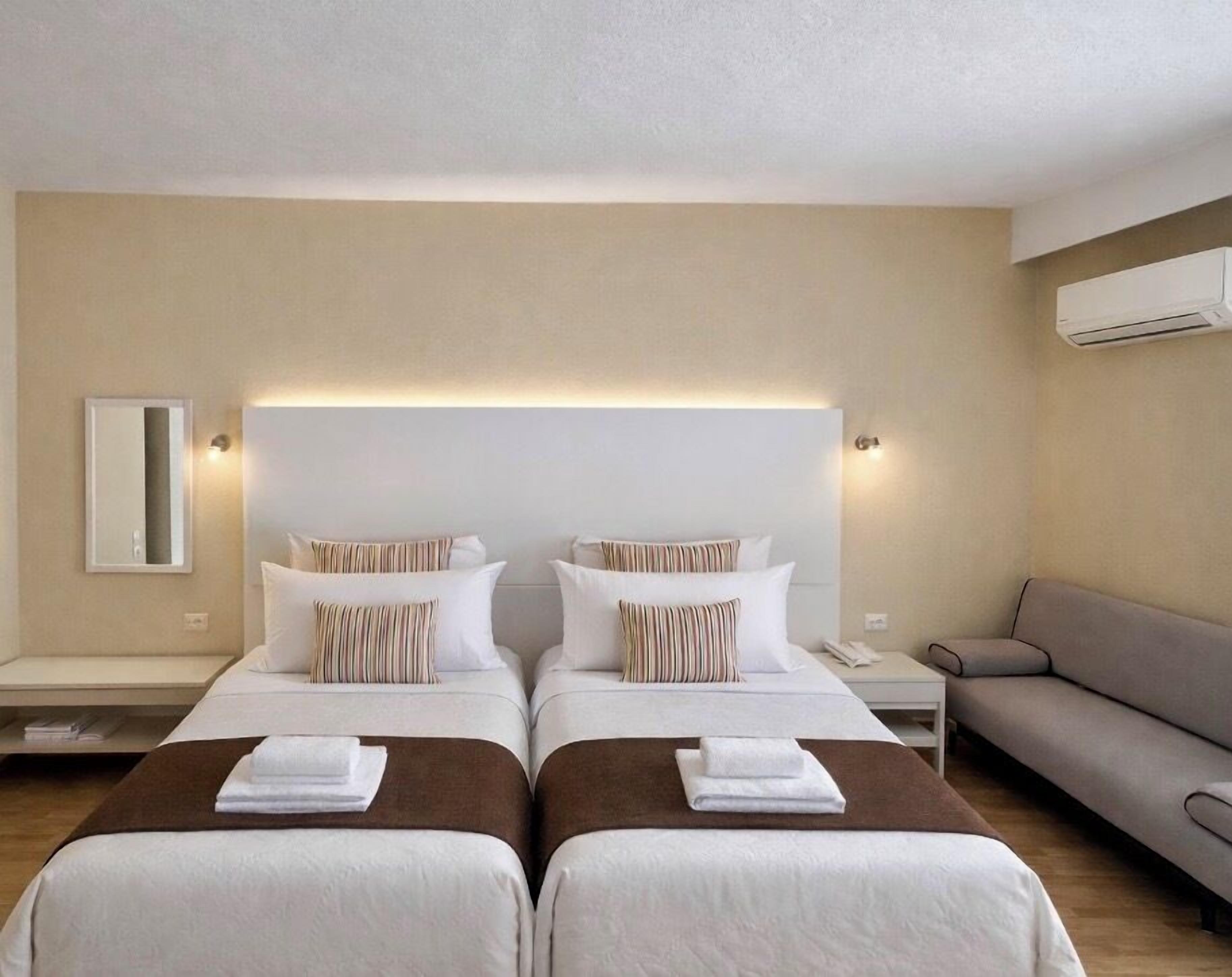 A hotel room with two beds, a sofa, and a mirror.
