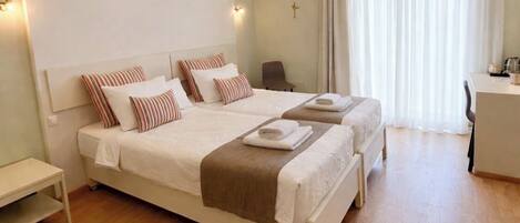 A double bed with a headboard, a bedside table, an air conditioning unit, a desk with a chair, and a window with curtains.
