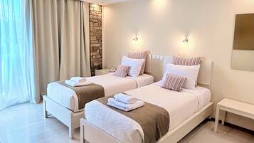 A hotel room with two beds, a stone accent wall, and a large window with curtains.