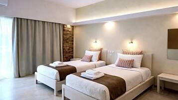 Una habitación de hotel moderna con dos camas individuales, una pared de acento de piedra y un ventanal con cortinas.