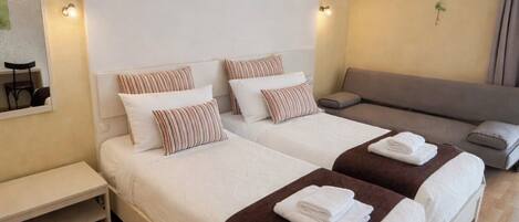 A hotel room with two beds, a sofa, a bench, and an air conditioning unit on the wall.