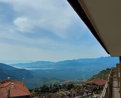 Vista desde un balcón sobre un paisaje montañoso con un lago y colinas al distante.