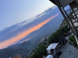 Un paisaje montañoso con un atardecer, una estructura con forma de tienda blanca, coches aparcados y una persona caminando.