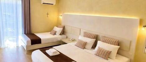 A hotel room with two beds, a large window with curtains, an air conditioning unit, and a bedside table with a phone.