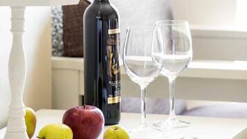 A table with a bottle of wine, two glasses, a bowl of apples, and a tray with utensils.