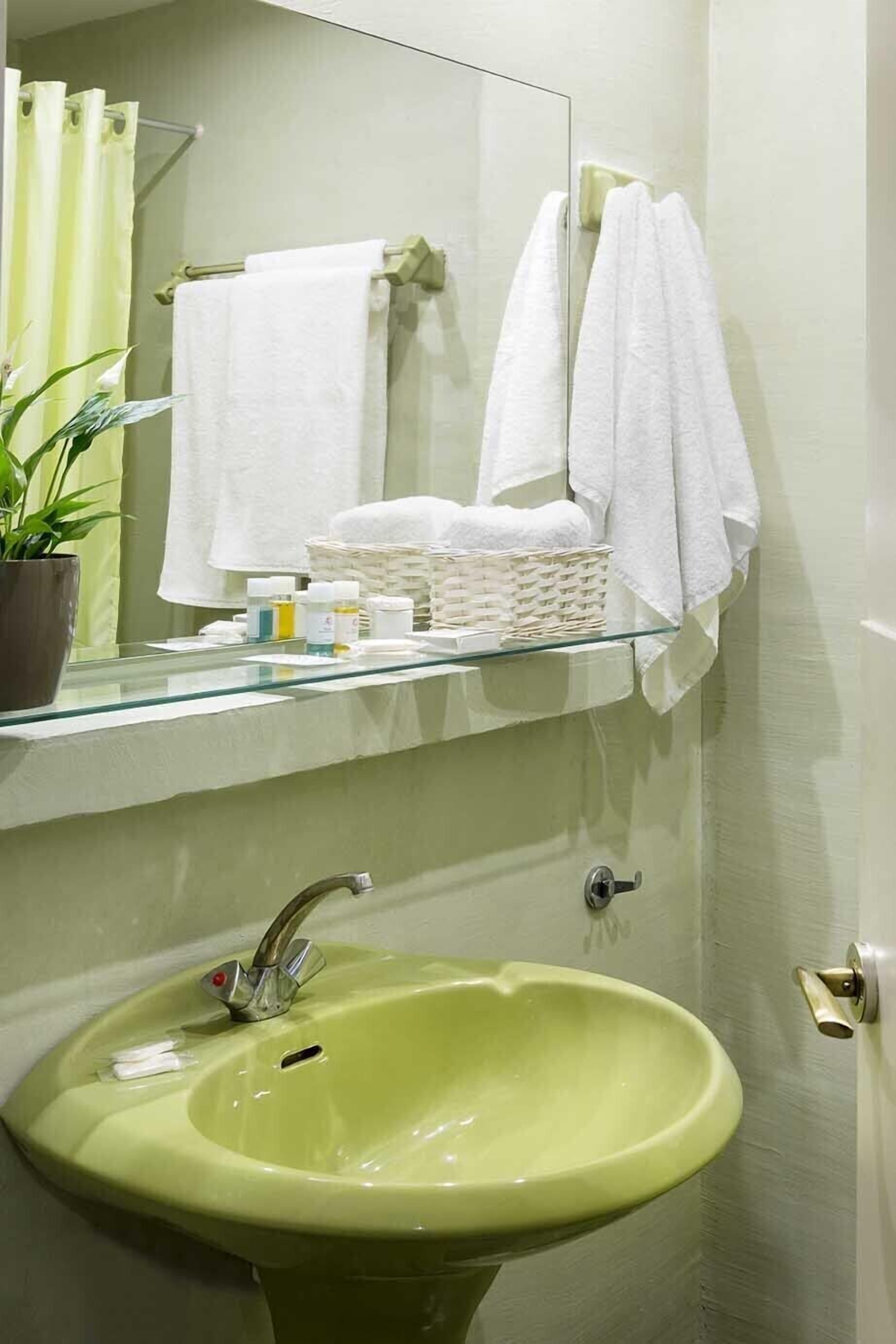 A bathroom with a green sink, a mirror, and a shelf with towels and toiletries.