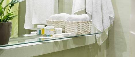 A bathroom with a green sink, a mirror, and a shelf with towels and toiletries.