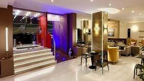 Un interior moderno con una escalera que lleva a un balcón, una zona de estar con sofás y una mesa de centro, y un espejo grande que refleja la habitación.