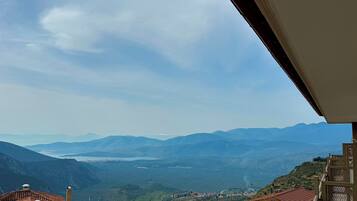 Vista desde un balcón sobre un valle con montañas a lo lejos, una masa de agua y un pueblo pequeño abajo.