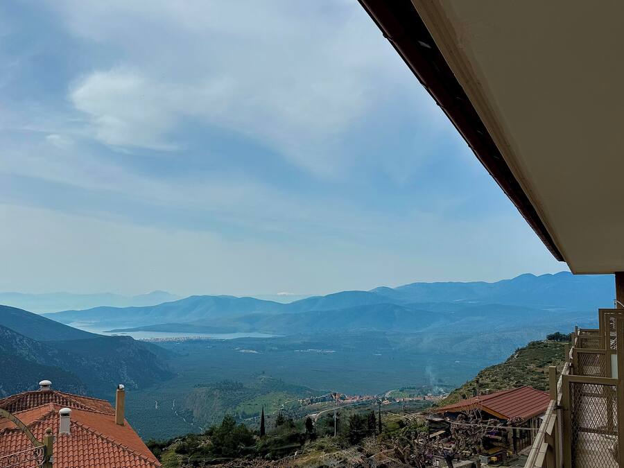 Vista desde un balcón sobre un valle con montañas a lo lejos, una masa de agua y un pueblo pequeño abajo.