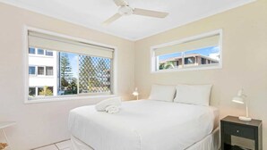 A bedroom with a bed, a nightstand, a ceiling fan, and two windows. - Superb 1 Bedroom Apartment Near the Beach (Burleigh Heads)
