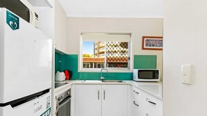 A compact kitchen with white cabinets, a microwave, a sink, and a window with a view of a building. - Superb 1 Bedroom Apartment Near the Beach (Burleigh Heads)