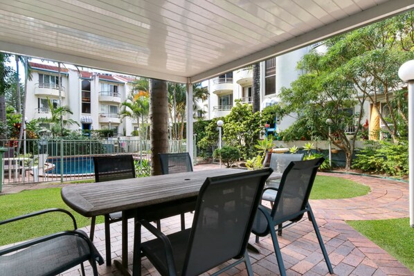Un espace extérieur aménagé en terrasse, avec une table et des chaises, une piscine et une vue sur un immeuble d’habitation.