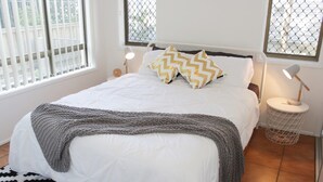 Een net opgemaakt bed met witte lakens en een grijze deken, twee bedlampjes en een kamerbreed tapijt met dessin.