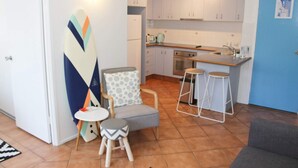 Een compacte keuken met witte kastjes, een blauwe deur en een klein eethoekje met een stoel en krukken.