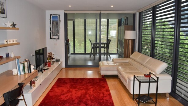 Un salon moderne avec un canapé, un tapis rouge, un téléviseur et un coin repas comprenant une table et des chaises.