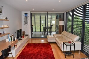 A modern living room with a sofa, a red rug, a TV, and a dining area with a table and chairs.