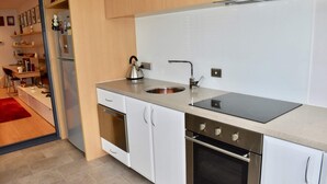Une cuisine moderne avec des meubles blancs, un évier en acier inoxydable, une bouilloire et un four.