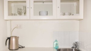 A kitchen with a stainless steel sink, a kettle, and cabinets containing glassware and dishes. - 1 Bedroom Studio Apartment near Eagle Street (Brisbane)