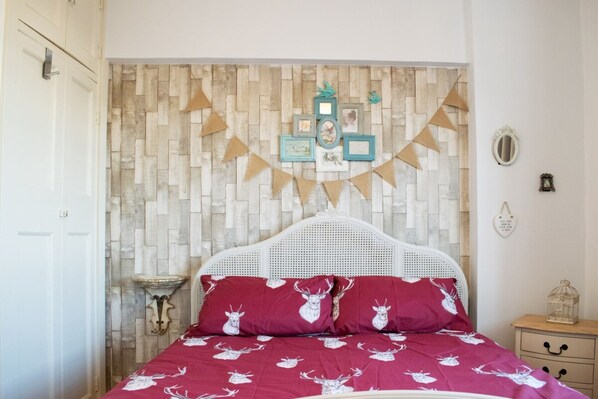 A bedroom with a bed, a wall-mounted shelf, and a bedside table with a lamp. - Beautifully Decorated Contemporary 2 Bedroom Flat (London)