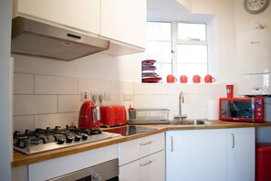 A kitchen with white cabinets, a gas stove, a red toaster, and a microwave. - Beautifully Decorated Contemporary 2 Bedroom Flat (London)