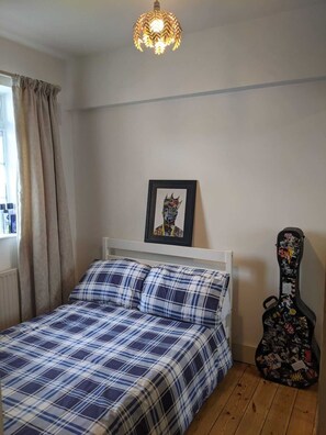A bedroom with a bed, a framed artwork, a guitar, and a unique ceiling light fixture. - Beautifully Decorated Contemporary 2 Bedroom Flat (London)