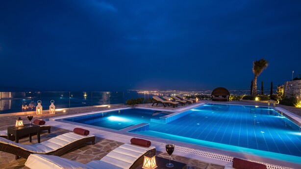 A rooftop infinity pool with lounge chairs and a view of the city at night.