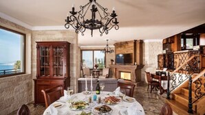 A dining room with a round table set for a meal, a chandelier, and a view of the sea.
