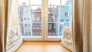 A room with a large window, a wooden floor, and a view of colorful buildings outside.