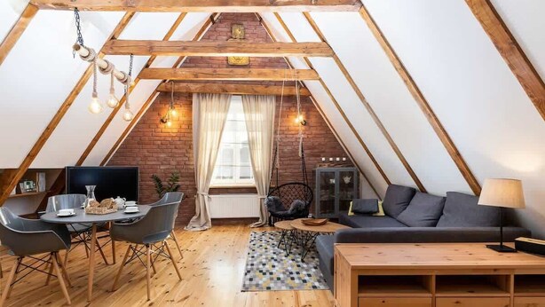 A cozy attic room with a dining area, sofa, and a TV.