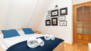 A bedroom with a bed, blue pillows, a wooden door, and framed pictures on the wall.
