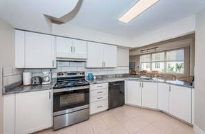Een moderne keuken met witte kasten, roestvrijstalen apparatuur en een groot raam dat voor natuurlijk licht zorgt.
