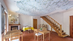 Uma sala de jantar com uma mesa e cadeiras de madeira, uma escada e piso ladrilhado.
