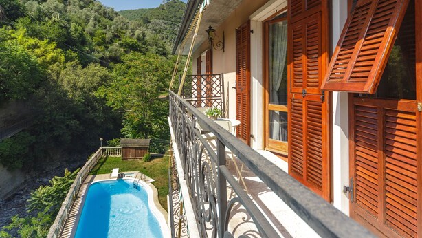 Uma varanda com piscina, persianas de madeira e vista para um morro verdejante.
