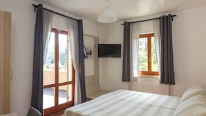 Um quarto com uma cama, televisão na parede e uma janela com cortinas.