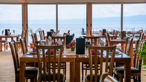 En restaurant med træborde og -stole, en menutavle og udsigt til havet.