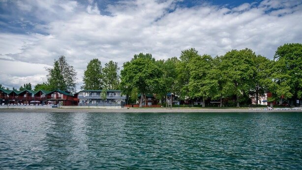 Et hotel ved vandet med flere bygninger, en sandstrand og frodige, grønne træer.