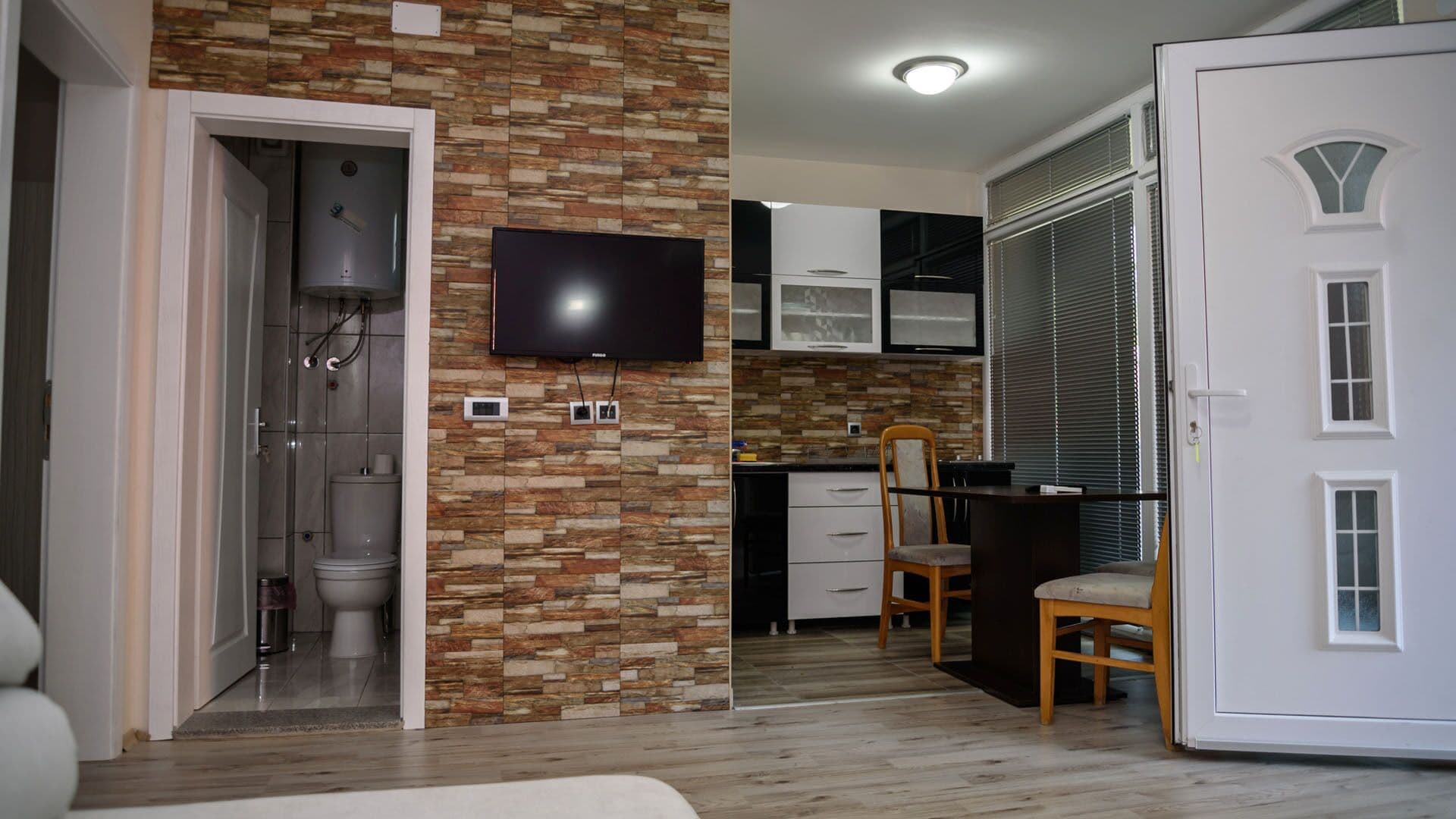 Een moderne keuken met een flatscreen televisie, houten kastjes en een eethoek met een houten tafel en stoelen.
