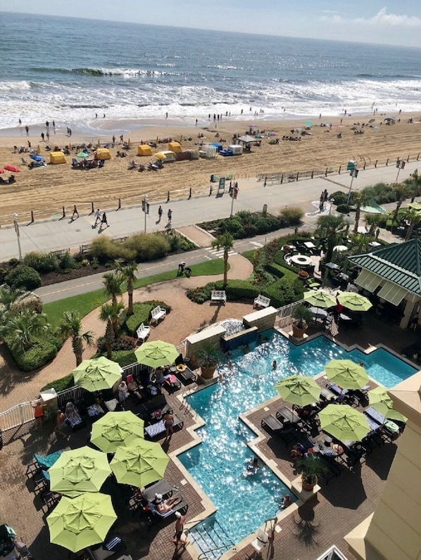 Un espace piscine agrémenté de parasols et de chaises longues, une plage en arrière-plan et une vue dégagée sur l’océan.