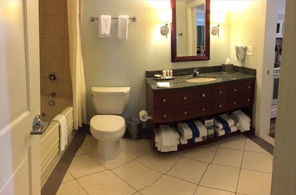 Un baño con inodoro, lavabo y ducha. Hay toallas colgadas en la pared y un espejo sobre el lavabo.