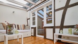 A cozy room with wooden flooring, a white sofa, and a small table with decorative items. There is a large window with a view of the outside. - Apartment in the half-timbered courtyard 'house in motion' (Neunkirchen-Seelscheid)